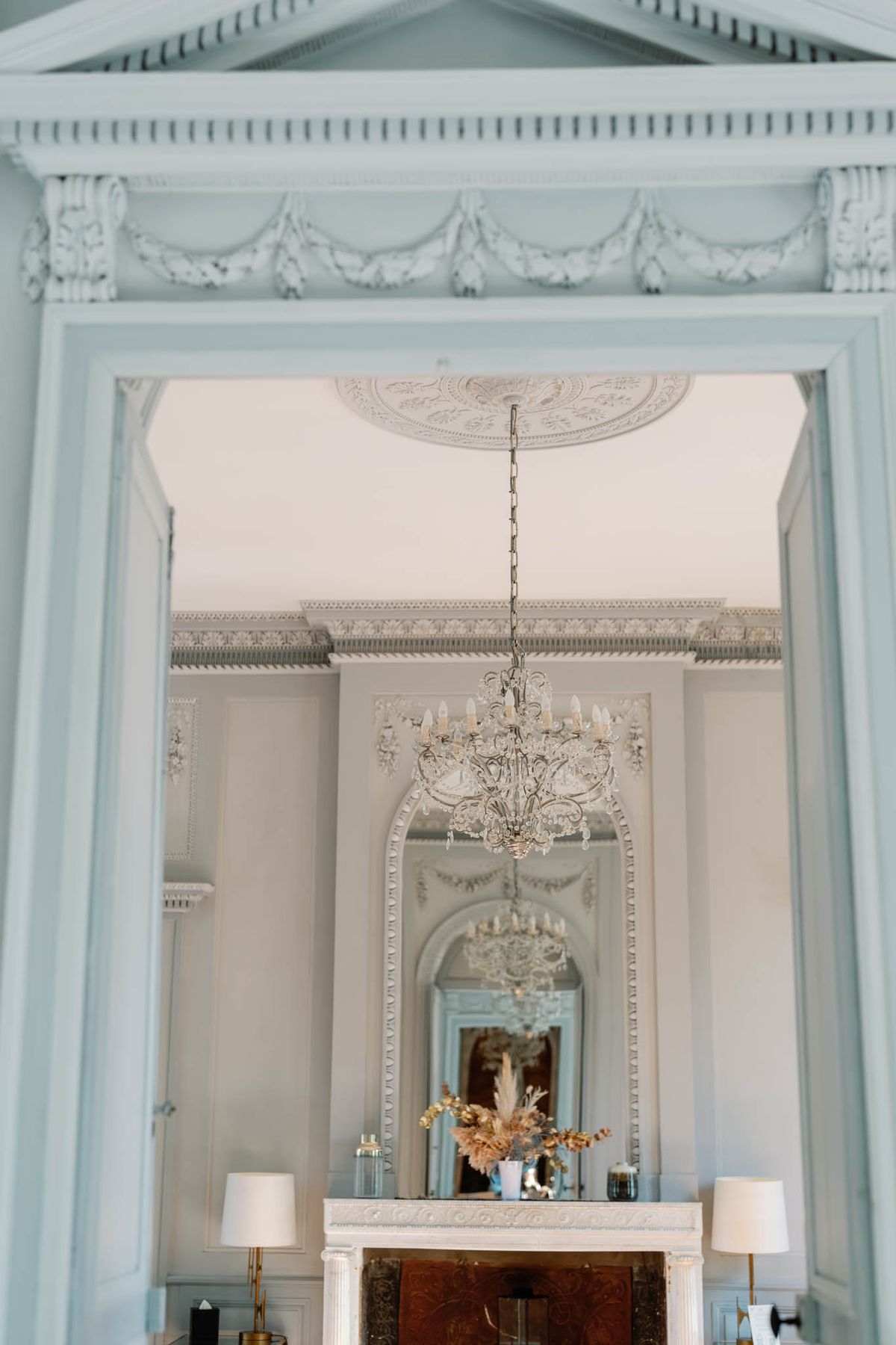 Doorway view of a formal reception room with crystal chandelier, stucco panelling and marble fireplace