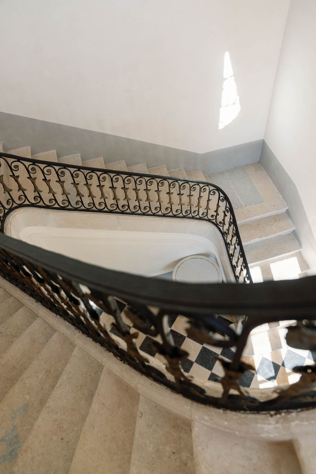 Grand stone staircase with wrought-iron balustrade and chequered tile landing at Château de l'Hospital