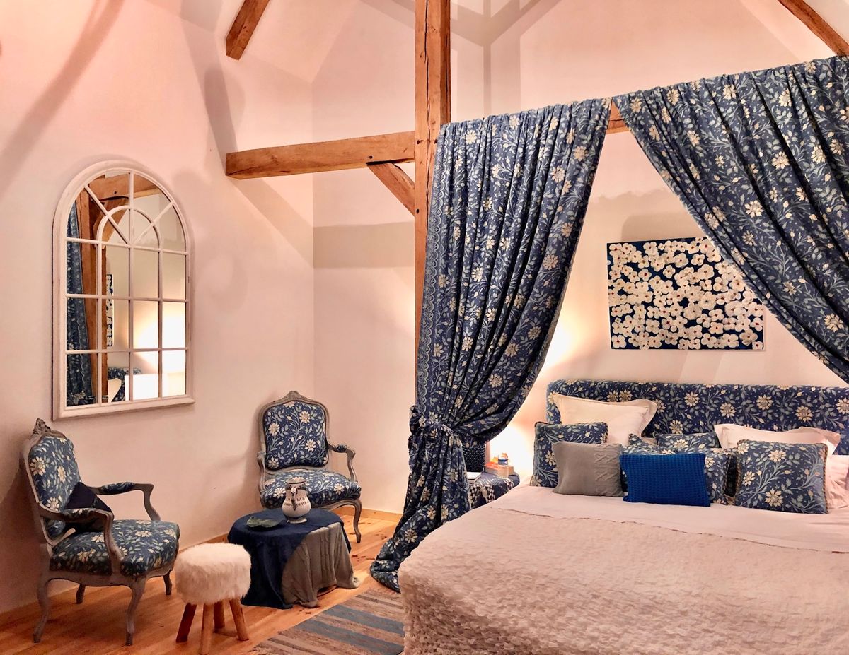 A guest bedroom with a blue floral canopied bed and matching armchairs beneath the roof beams