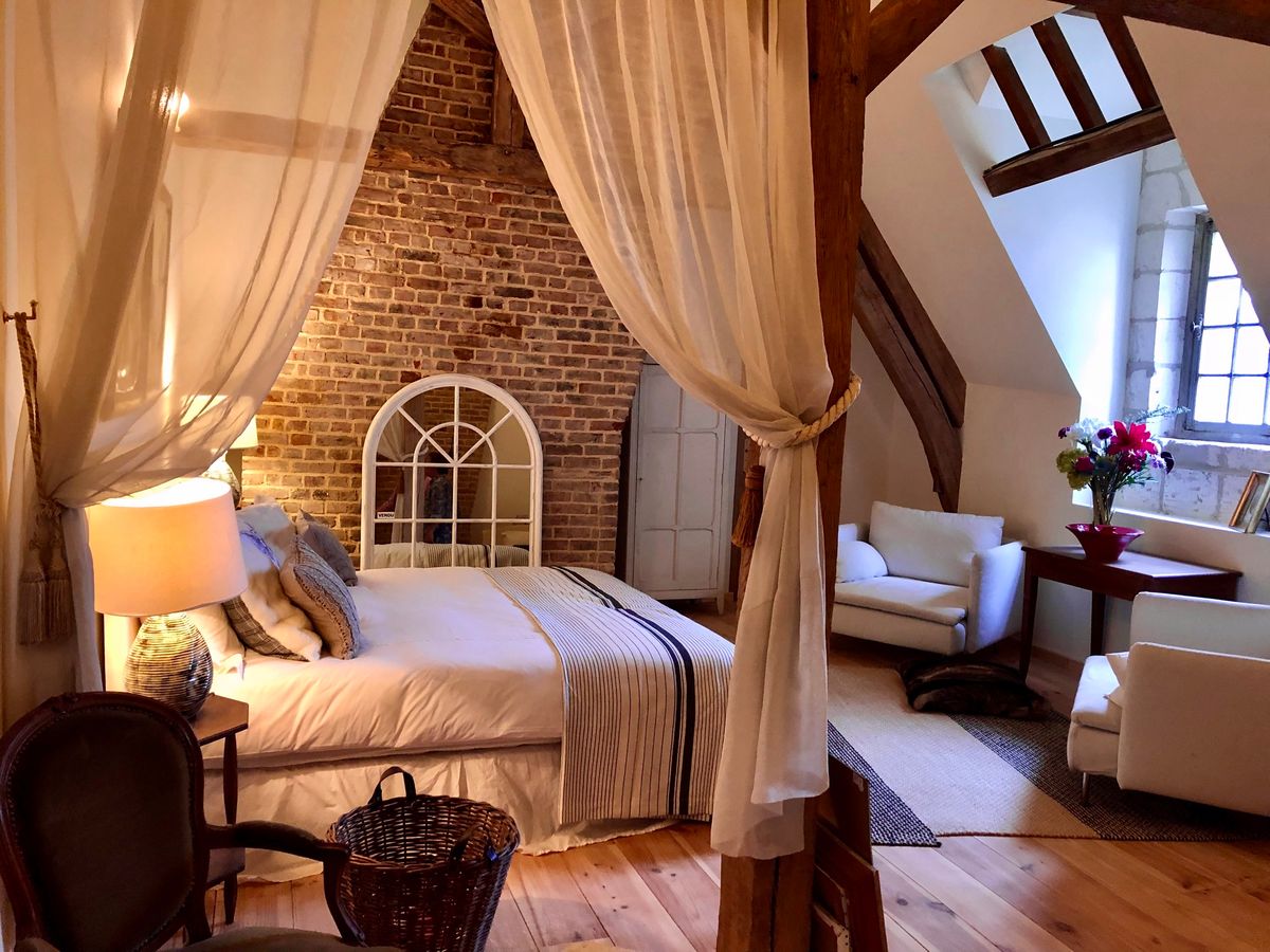 An attic guest room with a four poster bed, voile drapes and exposed brick and beams