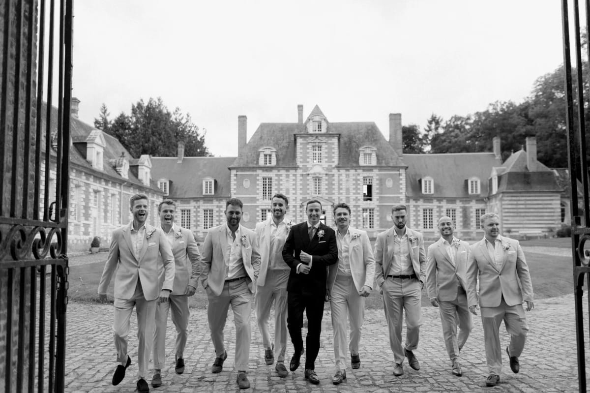 The groom and his party walking through the iron gates toward the château