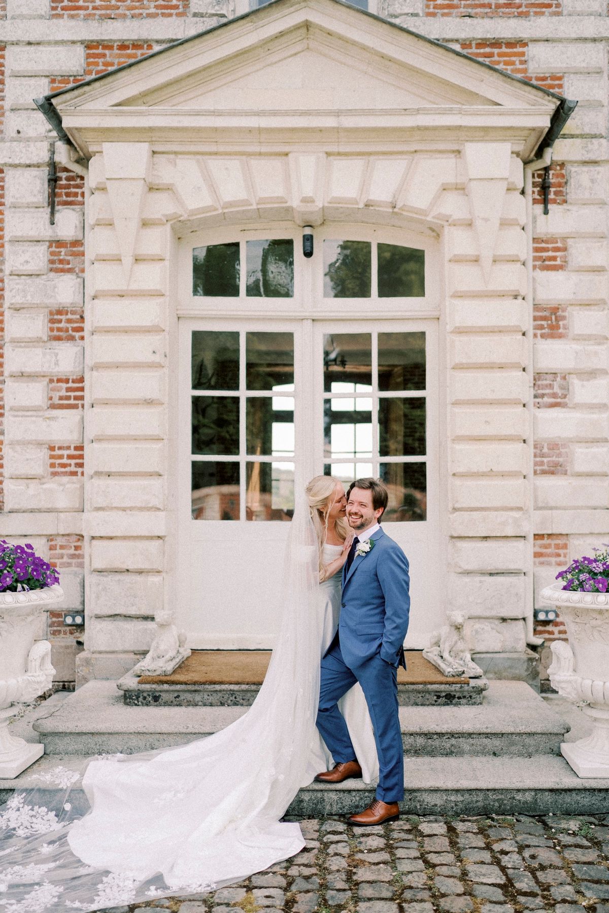 A couple on the stone porch steps of the château beside planted urns