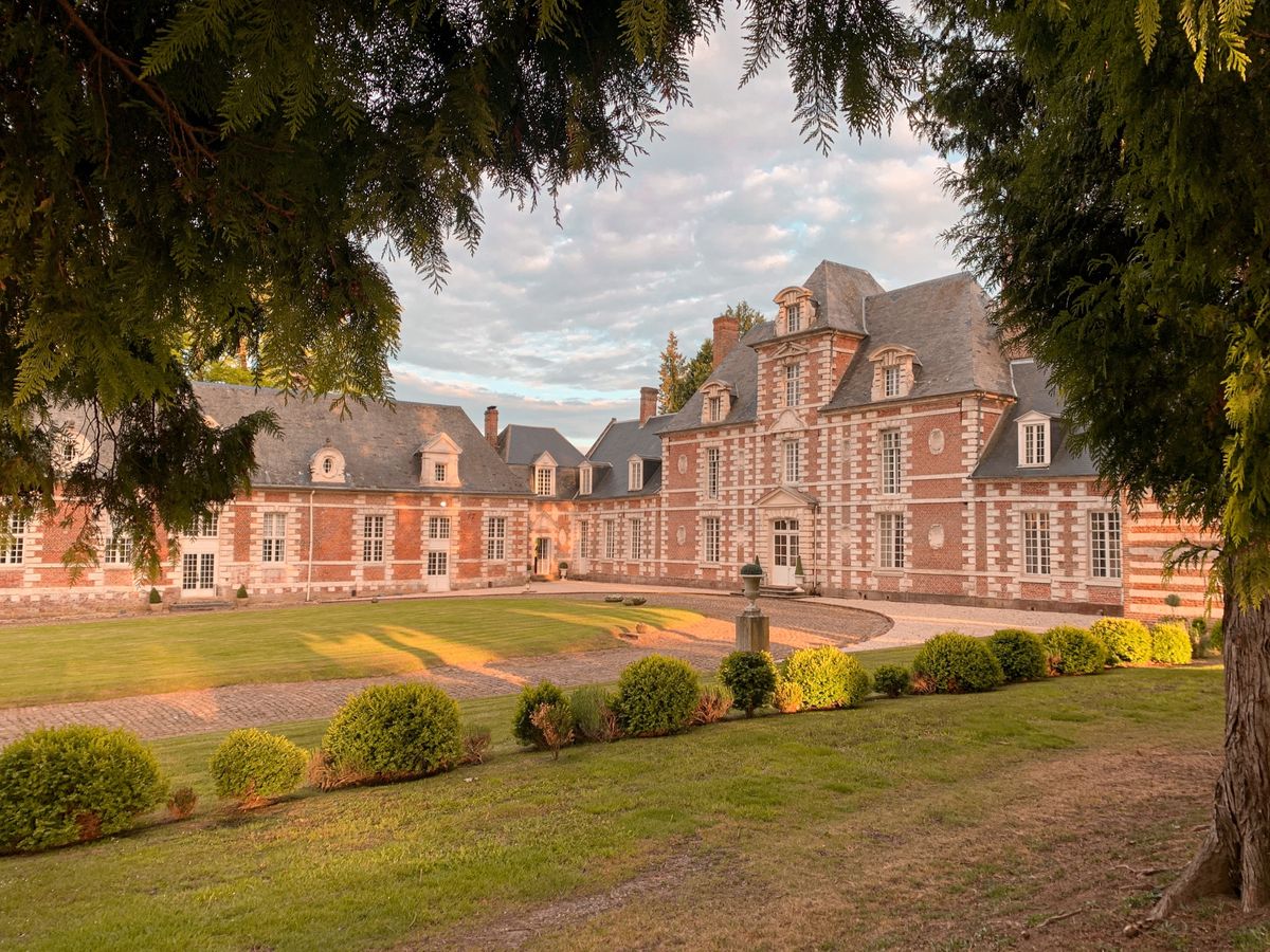 Château de Vauchelles and its long wing in golden evening light, framed by a cedar