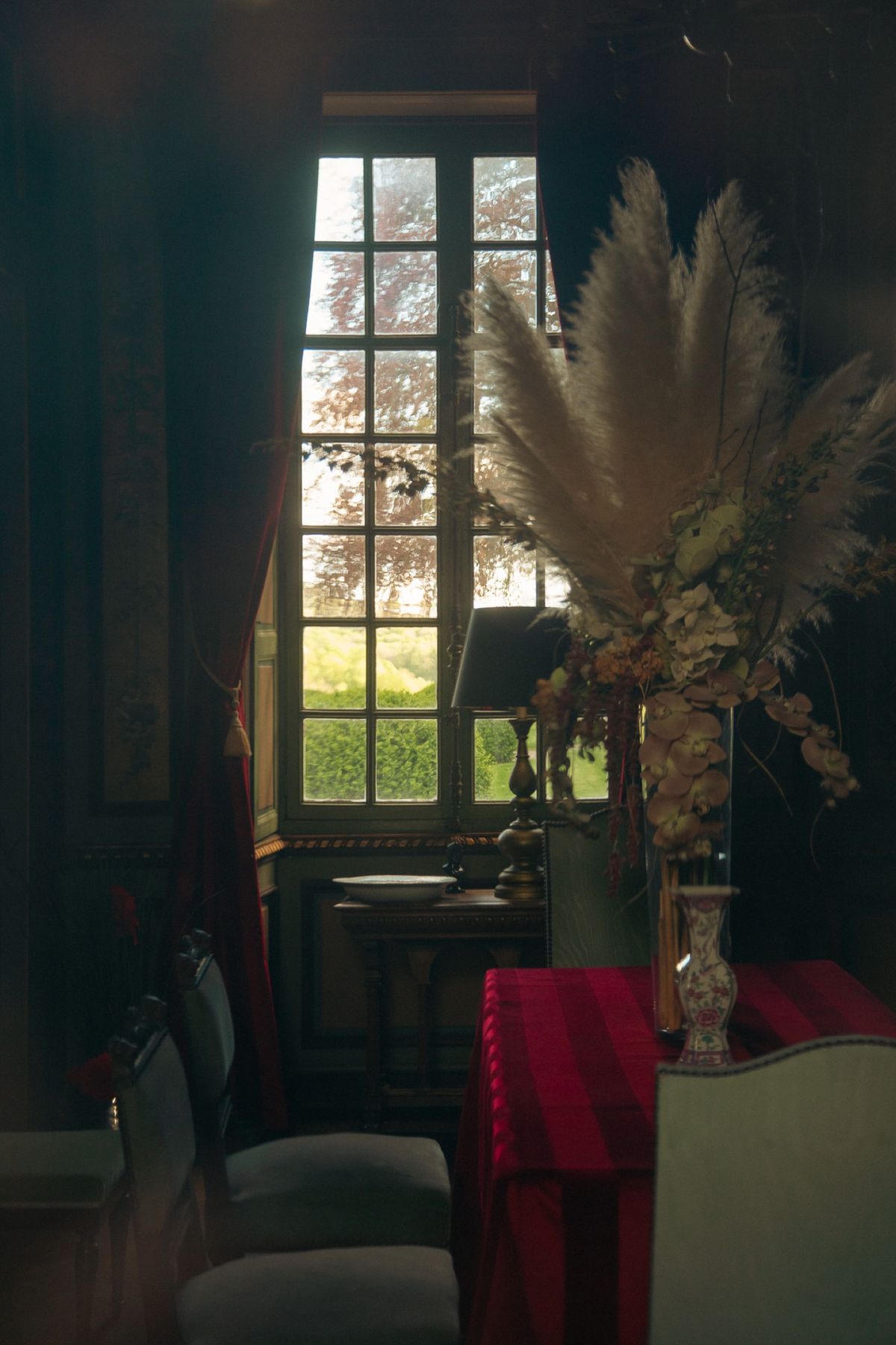 A tall window in a panelled room with a large dried flower arrangement
