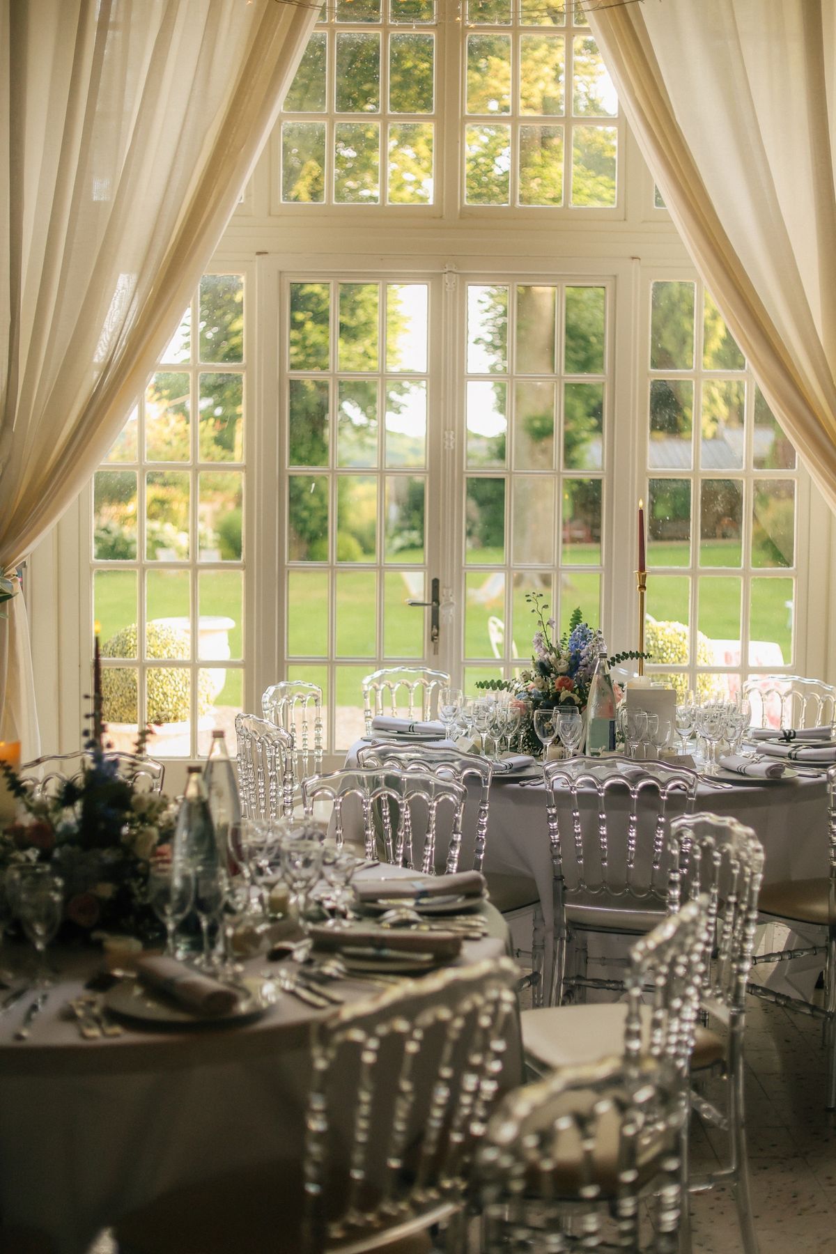 The garden room set for dinner with round tables and tall glazed doors opening to the lawn