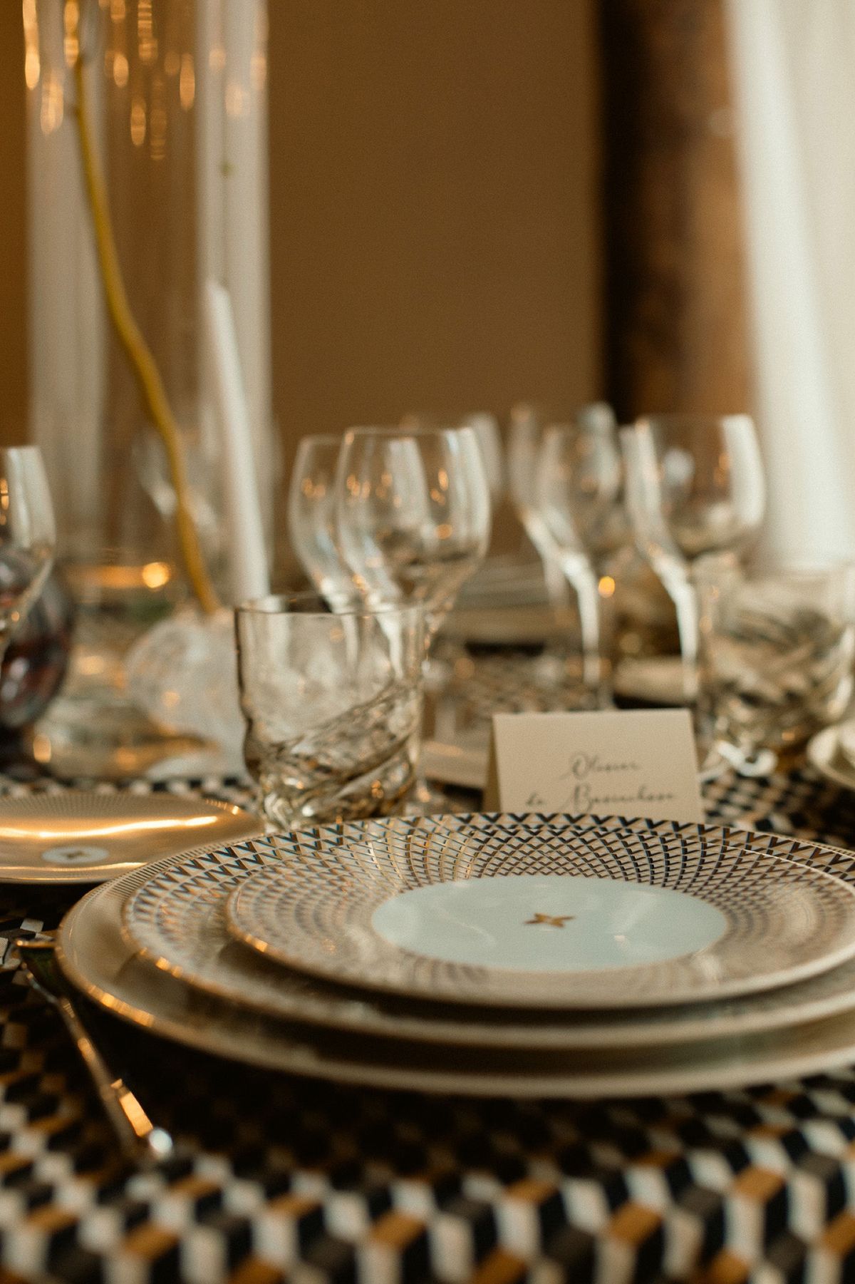 A place setting with a patterned charger, cut glassware and a handwritten place card