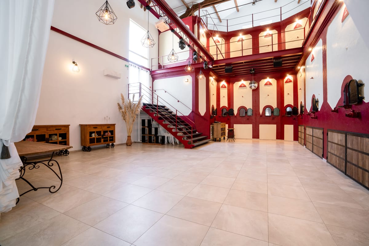 Industrial-chic reception hall with red and cream walls, former wine vats, a mezzanine and a tiled floor.