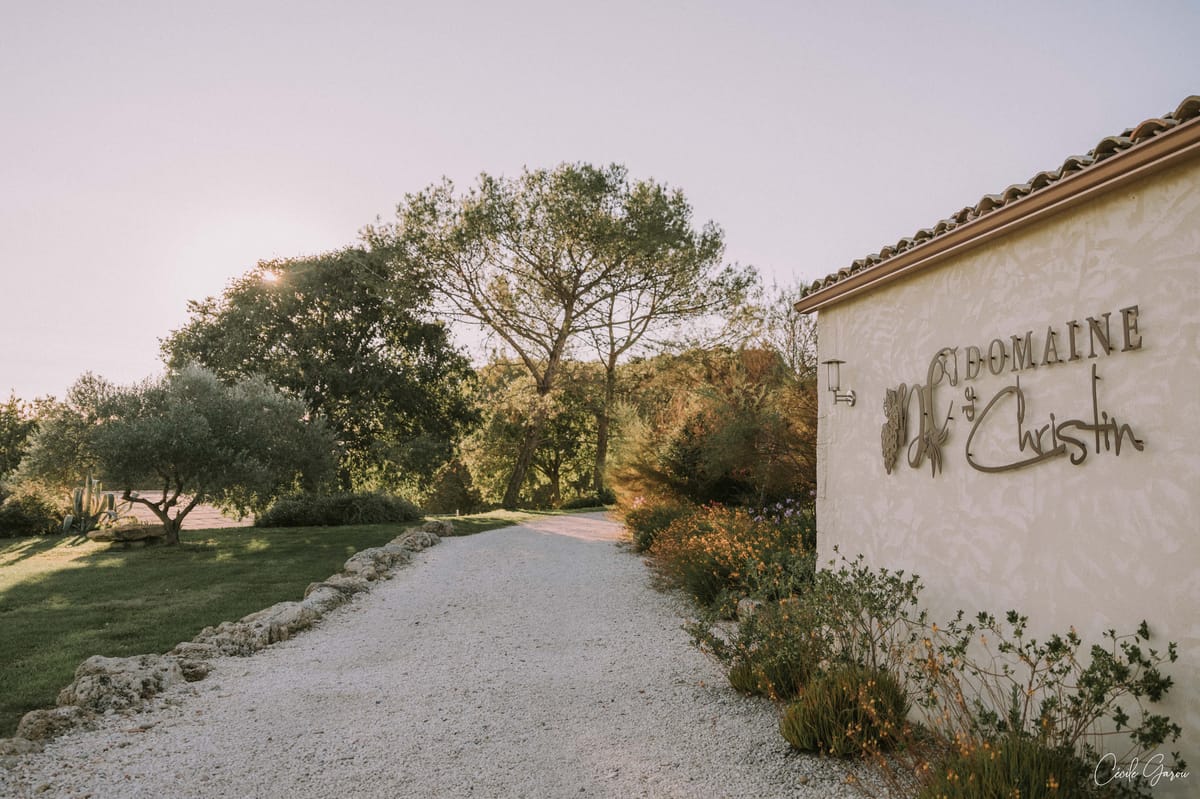 Gravel driveway at golden hour beside a wall bearing the Domaine de Christin sign.