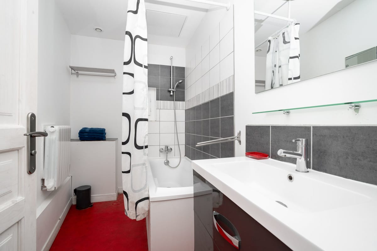 The bathroom of the Les Lauriers Roses gite, with a bath and shower, a wide white basin on a dark vanity and a mirrored shelf.