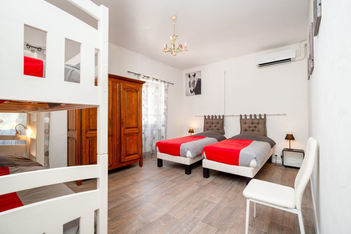 A bedroom in the Les Lauriers Roses gite with two single beds, a white bunk bed, a wooden wardrobe and a small chandelier.