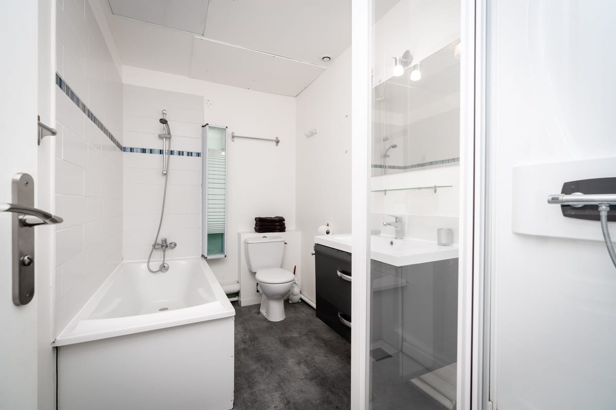 The bathroom of the Les Daims gite, with a bath and shower, a WC and a dark vanity unit with a basin and mirror.