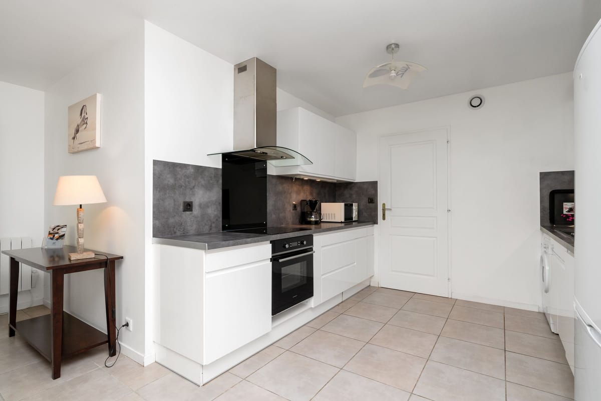 The fitted kitchen of the Les Daims gite, with white units, a grey splashback, an oven, a microwave and an extractor hood.