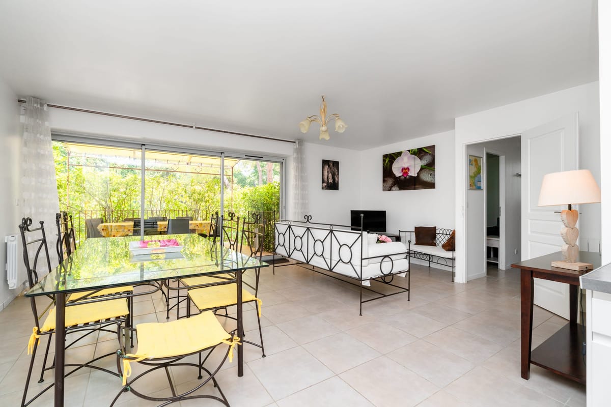 The open living and dining room of the Les Daims gite, with a glass-topped table, wrought-iron furniture and sliding doors onto the garden.