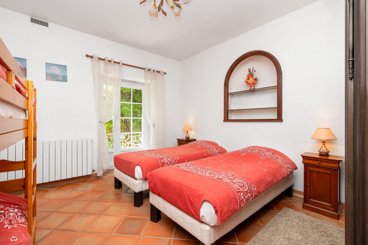 A bedroom in the Les Pins gite with two single beds, a bunk bed, a terracotta tiled floor and an arched wall niche.