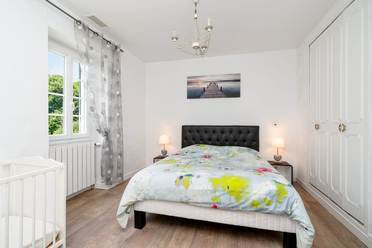 A bedroom in the Les Pins gite with a double bed, a cot, fitted wardrobes and a curtained window.
