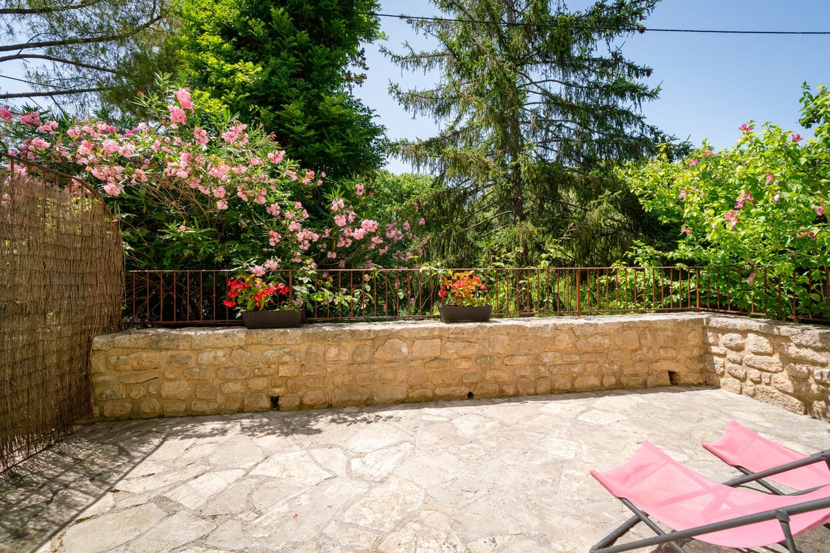 The private stone terrace of the Les Pins gite, with sun loungers, a low stone wall and oleander in flower.