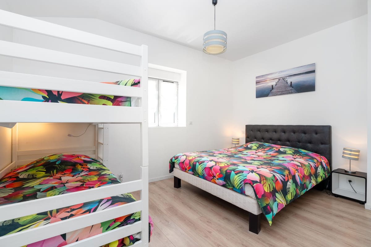 A bedroom in the Les Vignes gite with a double bed and a white bunk bed in bright printed covers.