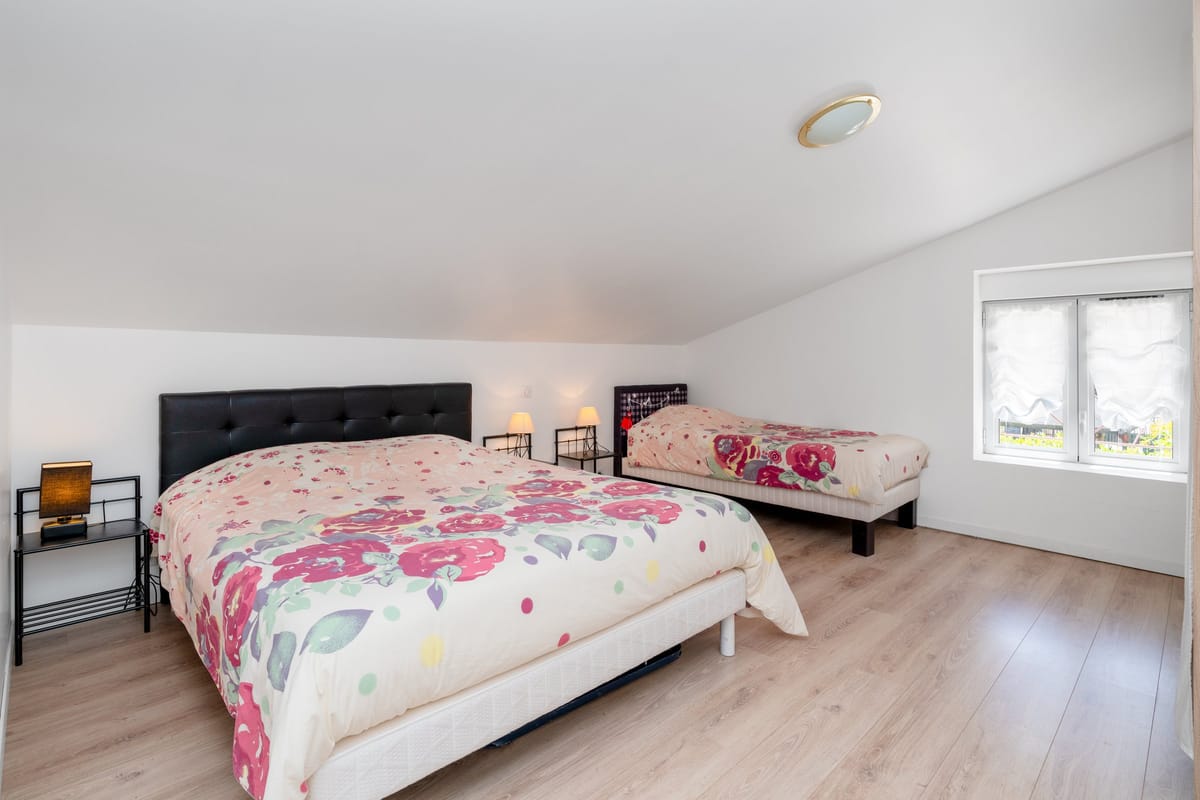 A bedroom in the Les Vignes gite set under a sloping ceiling, with a double bed and an additional single bed.