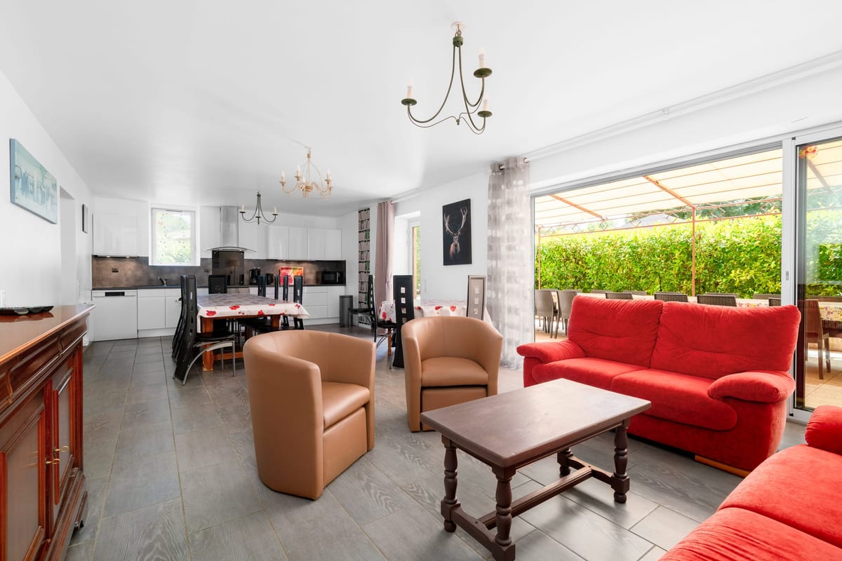 The open-plan living and dining room of the Les Vignes gite, with red sofas, a dining table, the kitchen beyond and sliding doors onto the terrace.