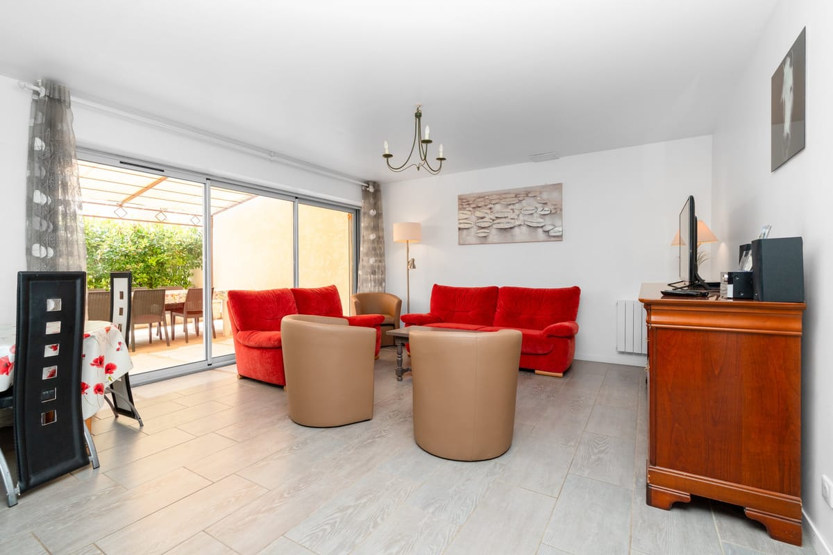 The lounge of the Les Vignes gite, with red sofas, tan tub chairs, a chandelier and sliding doors onto the shaded terrace.