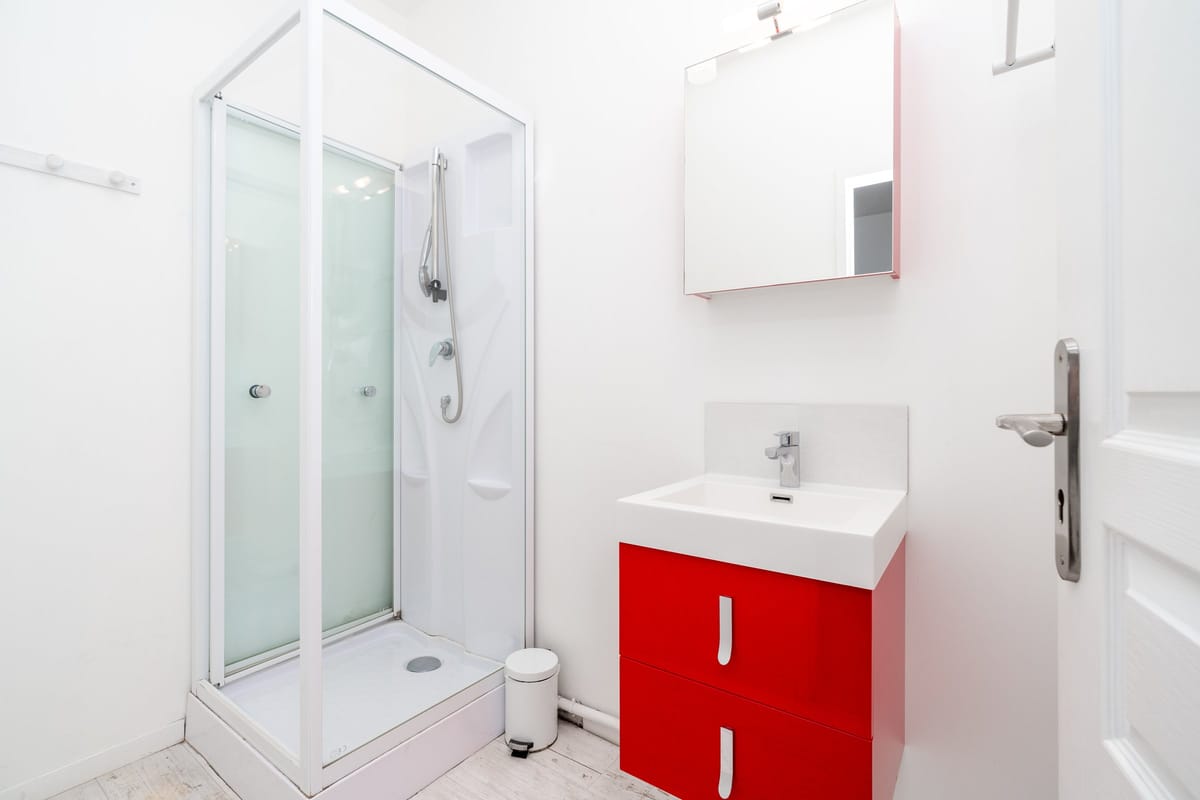 The upstairs shower room of the Les Vignes gite, with a corner shower cubicle and a red vanity unit with a basin and mirror.