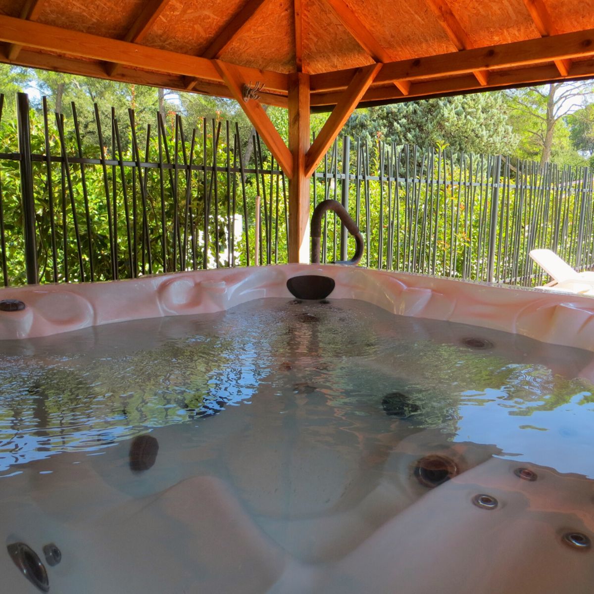 Outdoor whirlpool spa set under a timber gazebo surrounded by greenery.