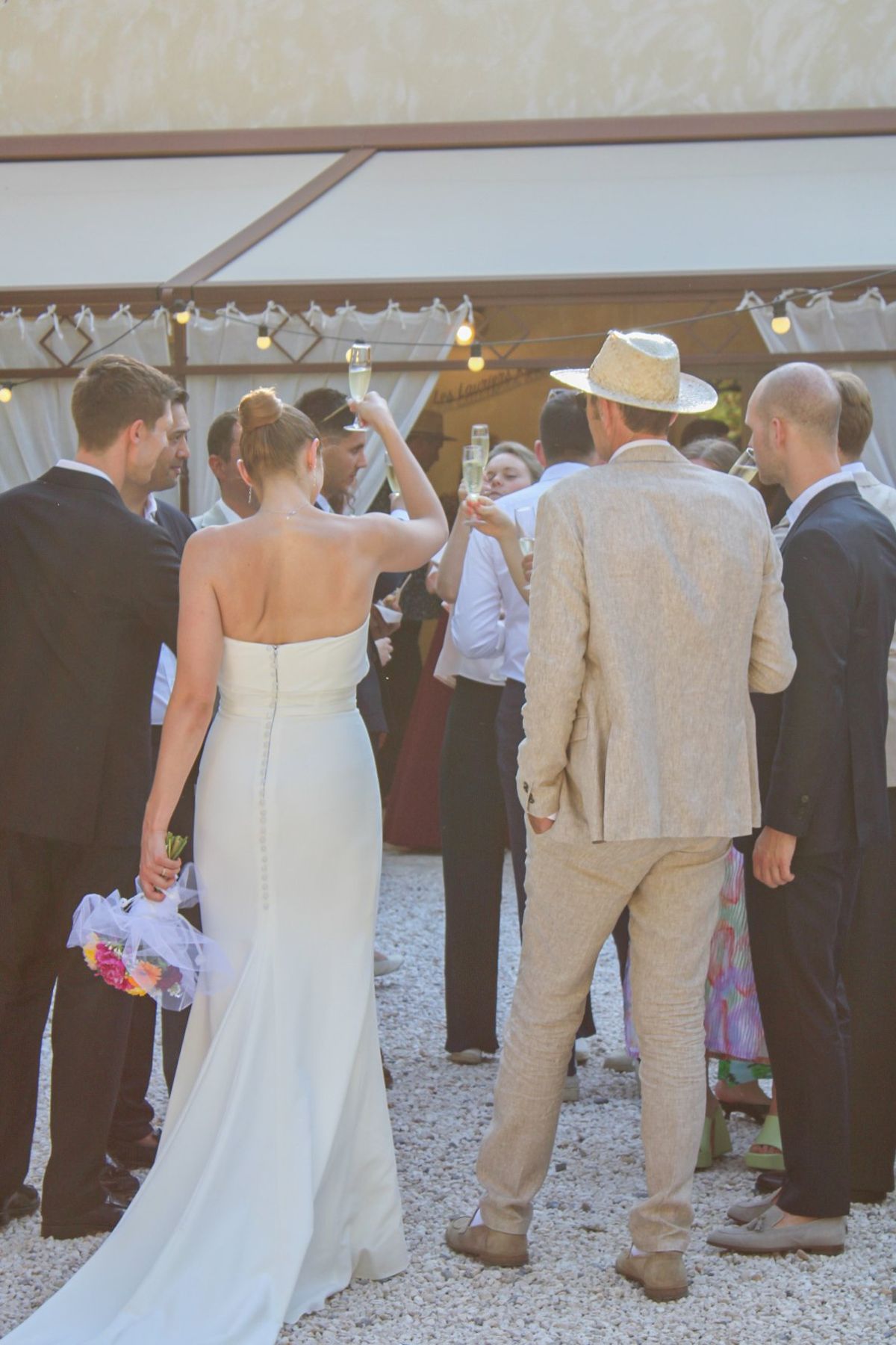 Guests raising glasses of champagne under a white marquee hung with festoon lights.