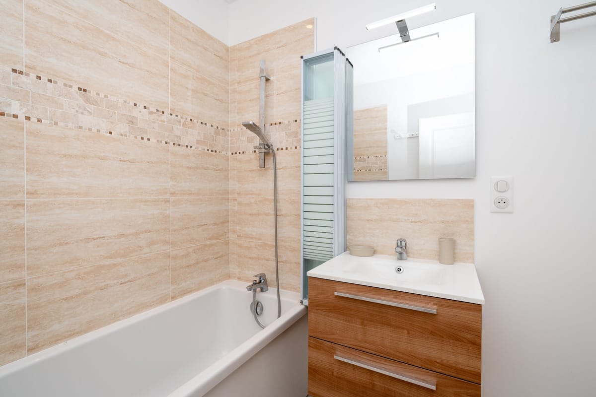 The bathroom of one of the estate studios, with a bath and shower, a wooden vanity with a basin and travertine tiling.