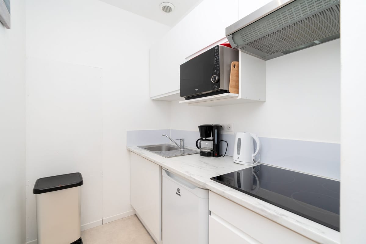 The kitchenette of one of the estate studios, with white units, an induction hob, a sink, a kettle and a coffee machine.