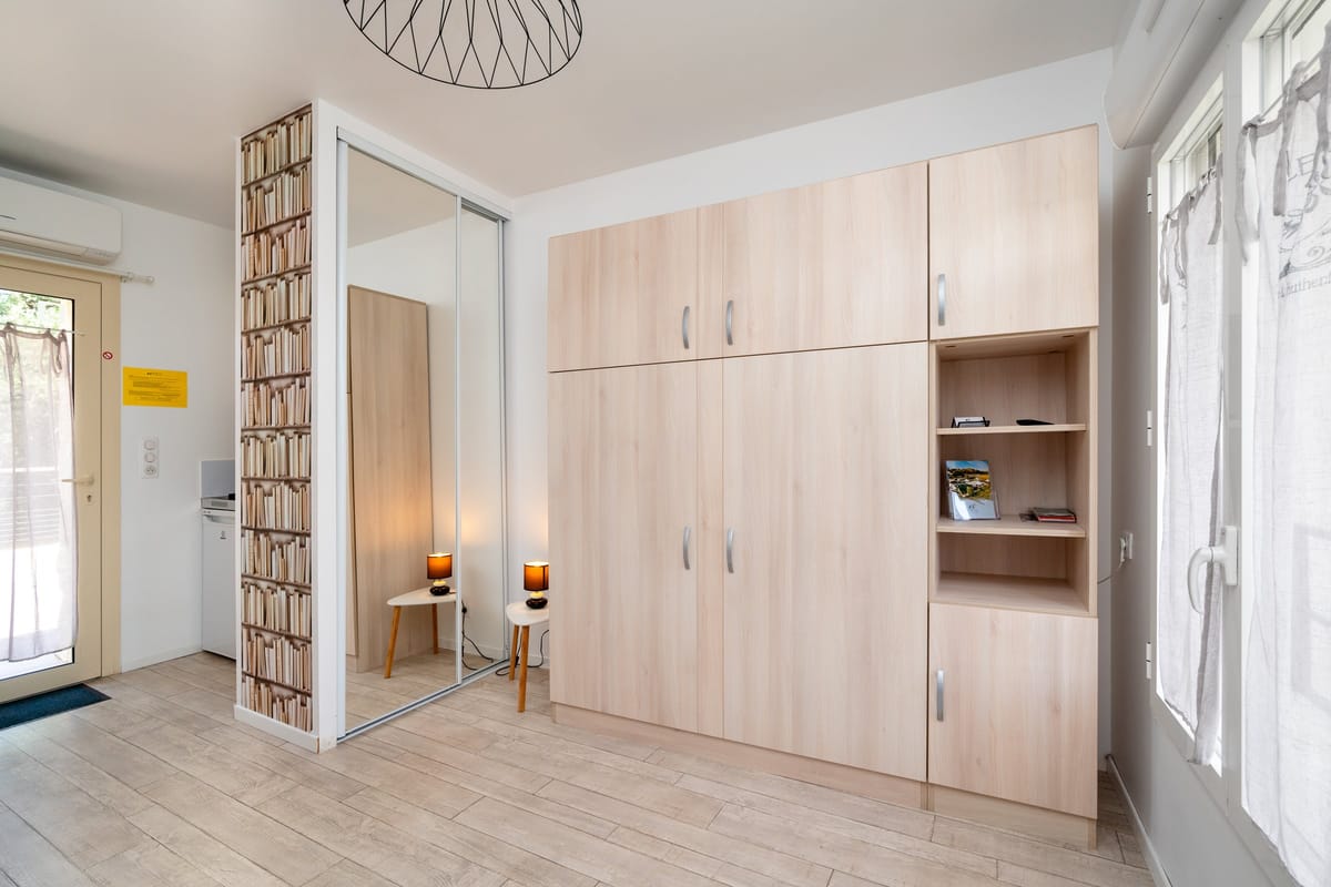 The interior of one of the estate studios, with fitted pale-wood wardrobes, a mirrored partition and a glazed door onto the outside.