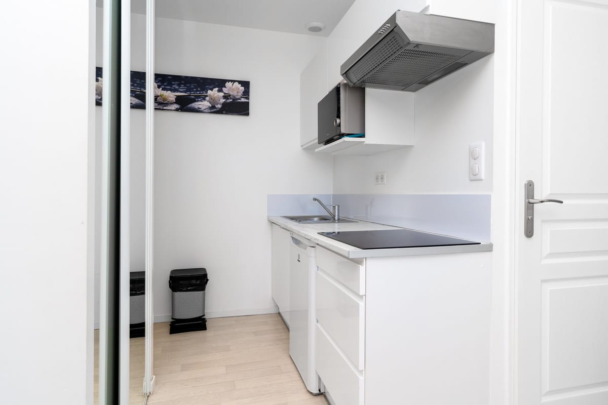 The kitchenette of another estate studio, with white units, an induction hob and extractor, beside a mirrored partition.