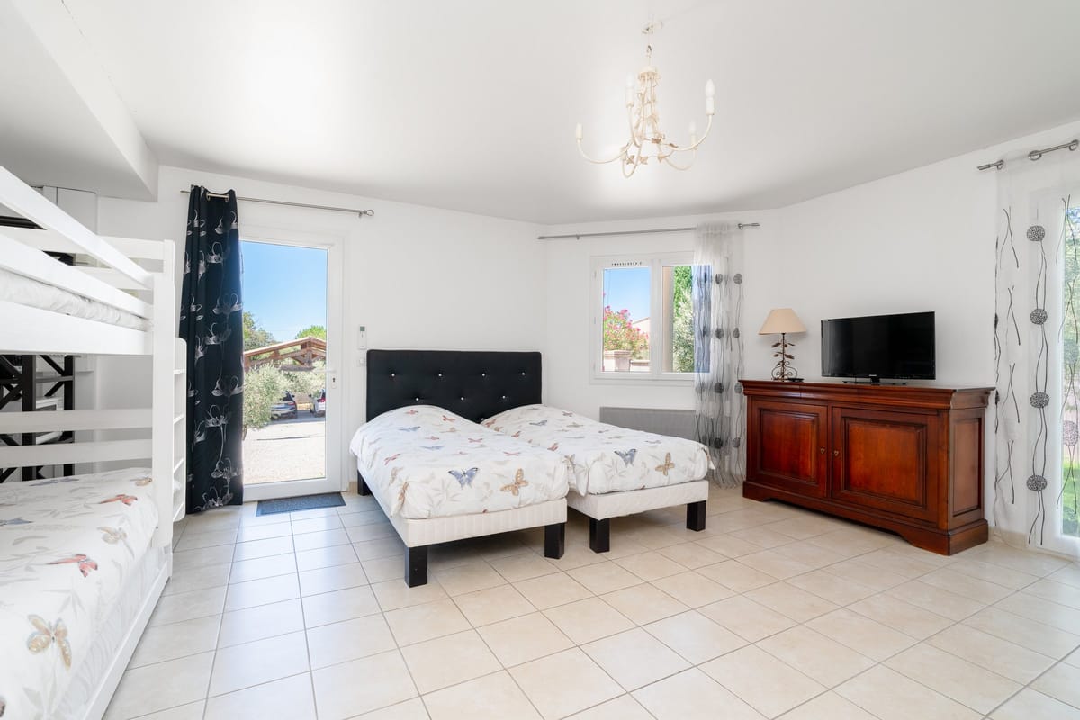 A bedroom in one of the private villas, with a double bed, bunk beds, a wooden chest of drawers and doors onto the garden.