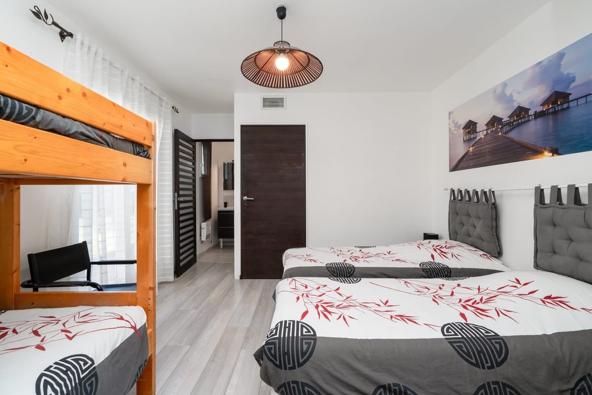 A bedroom in one of the private villas, with a double bed and a pine bunk bed beneath a woven pendant light.