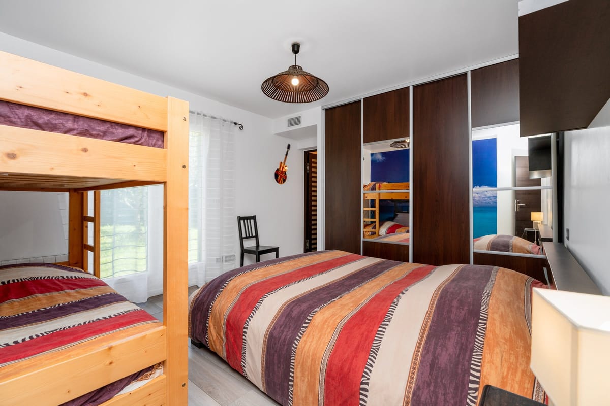 A bedroom in one of the private villas, with a double bed in striped covers, a pine bunk bed and fitted wardrobes.