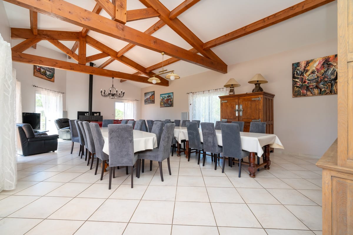 The dining room of one of the private villas, set with long tables and grey upholstered chairs beneath exposed timber trusses.