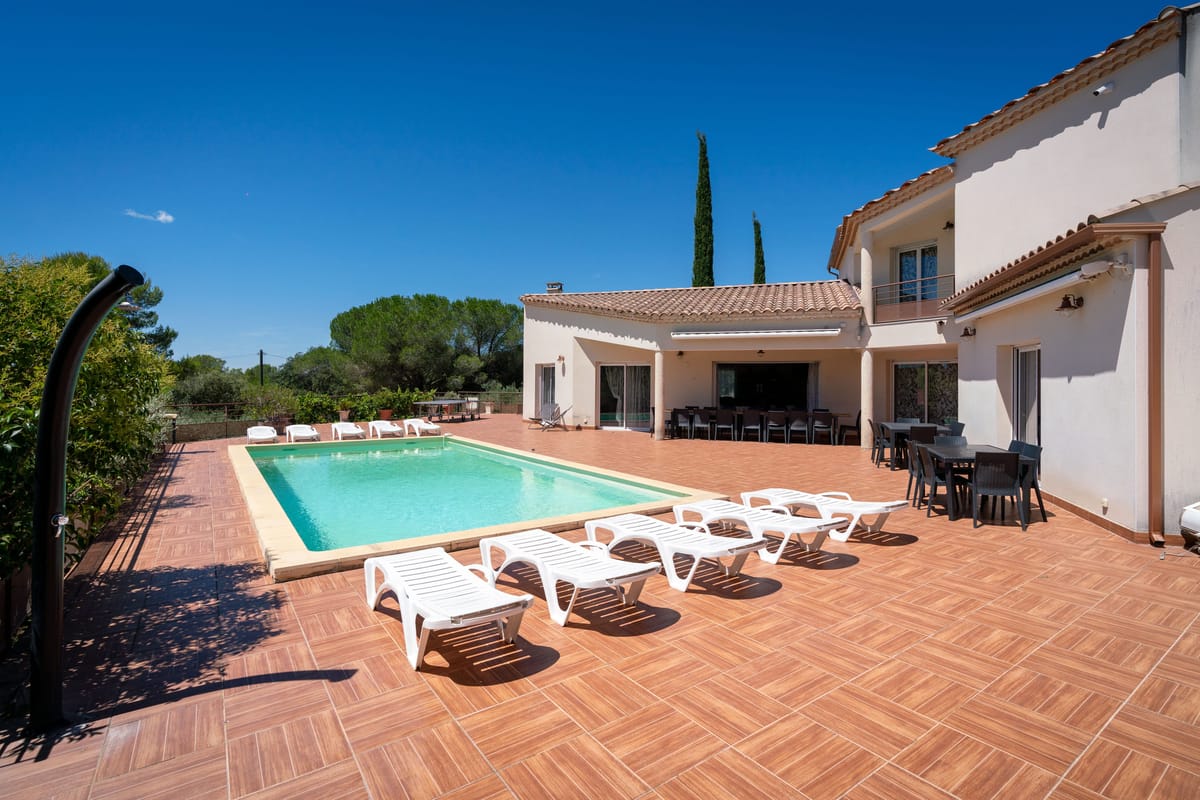 A two-storey villa with a private swimming pool, sun loungers and a tiled terrace under a blue sky.