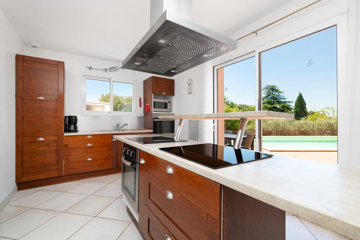 The kitchen of one of the private villas, with dark wood units and a central island with an induction hob, looking out towards the pool.