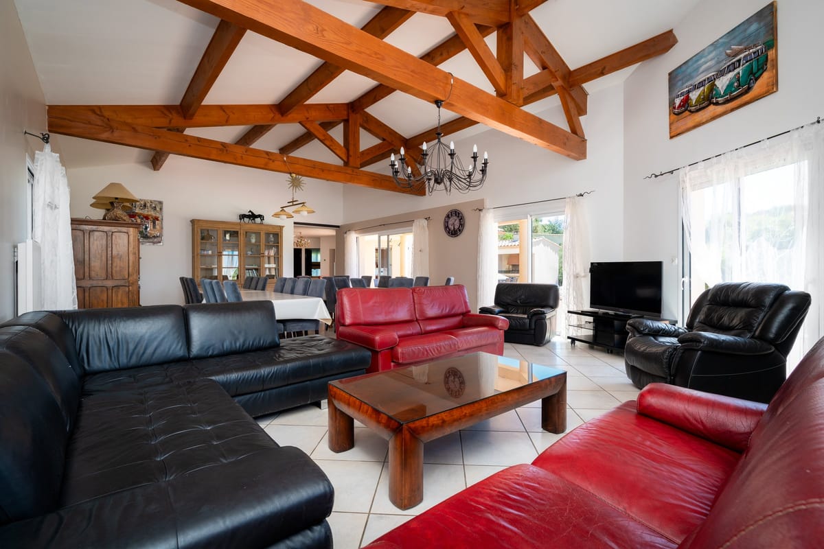 The open-plan living room of one of the private villas, with exposed timber roof trusses, black and red leather sofas and a dining area beyond.