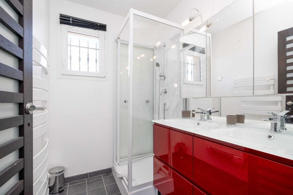 A shower room in one of the private villas, with a corner shower cubicle and a red gloss vanity with twin basins.