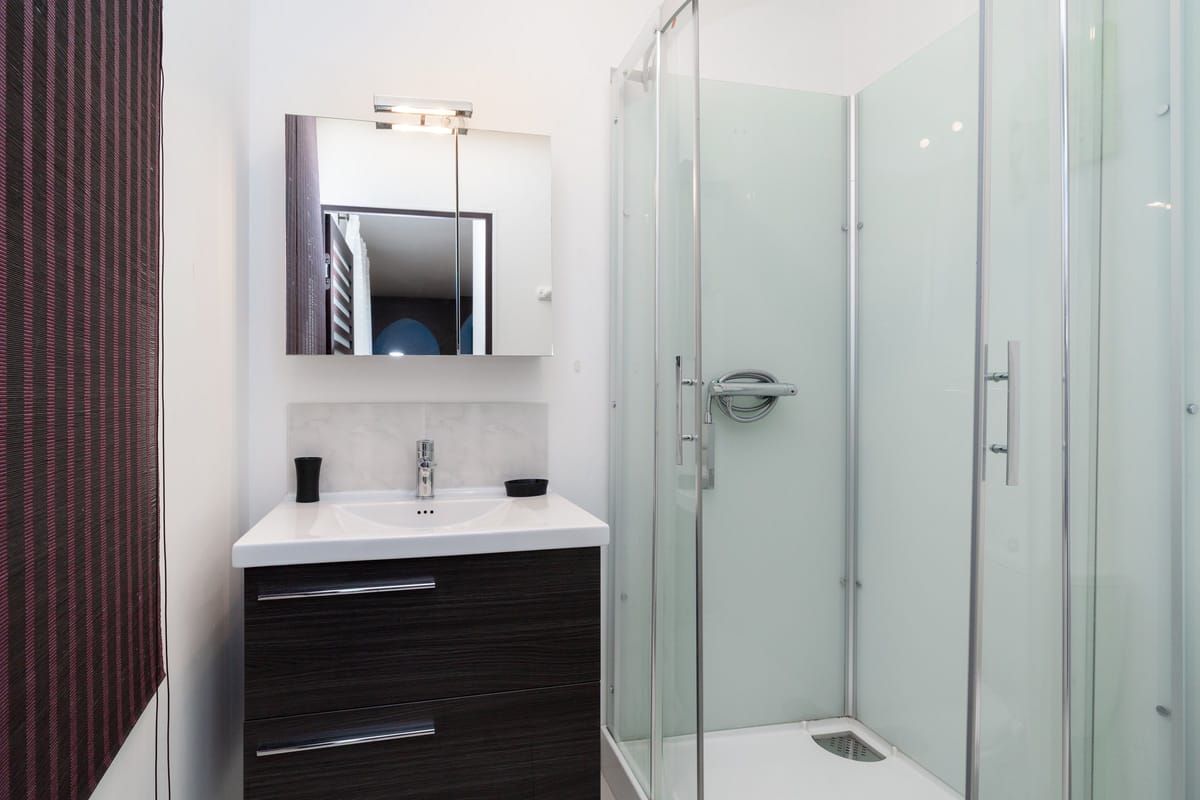 A shower room in one of the private villas, with a corner shower cubicle and a dark vanity with a basin and mirror.