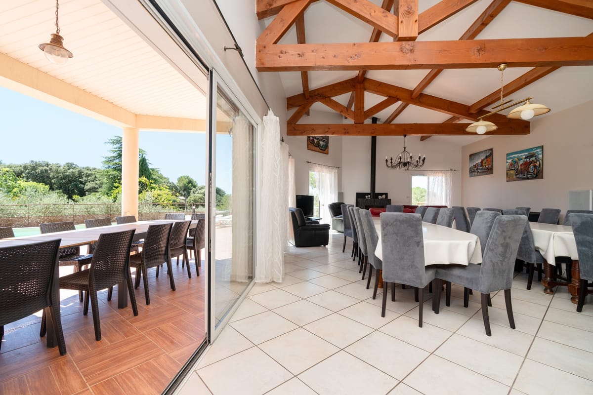 A covered terrace of one of the private villas, laid with a long table and opening through sliding doors into the indoor dining room.