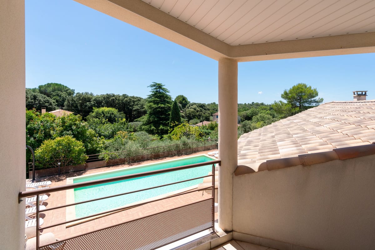 A covered first-floor terrace at one of the private villas, looking over the swimming pool to the wooded hills.