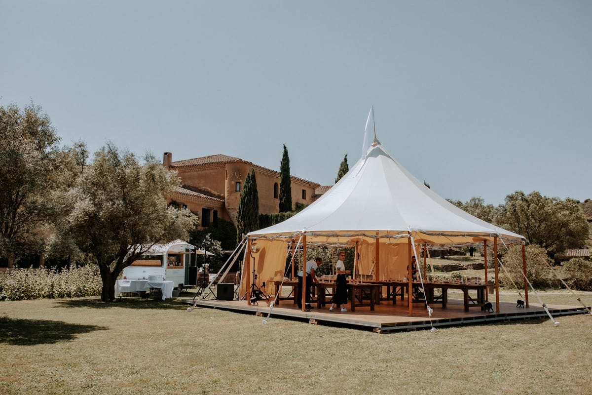 Sailcloth marquee on a timber deck set for a wedding reception, the ochre mas and cypresses behind