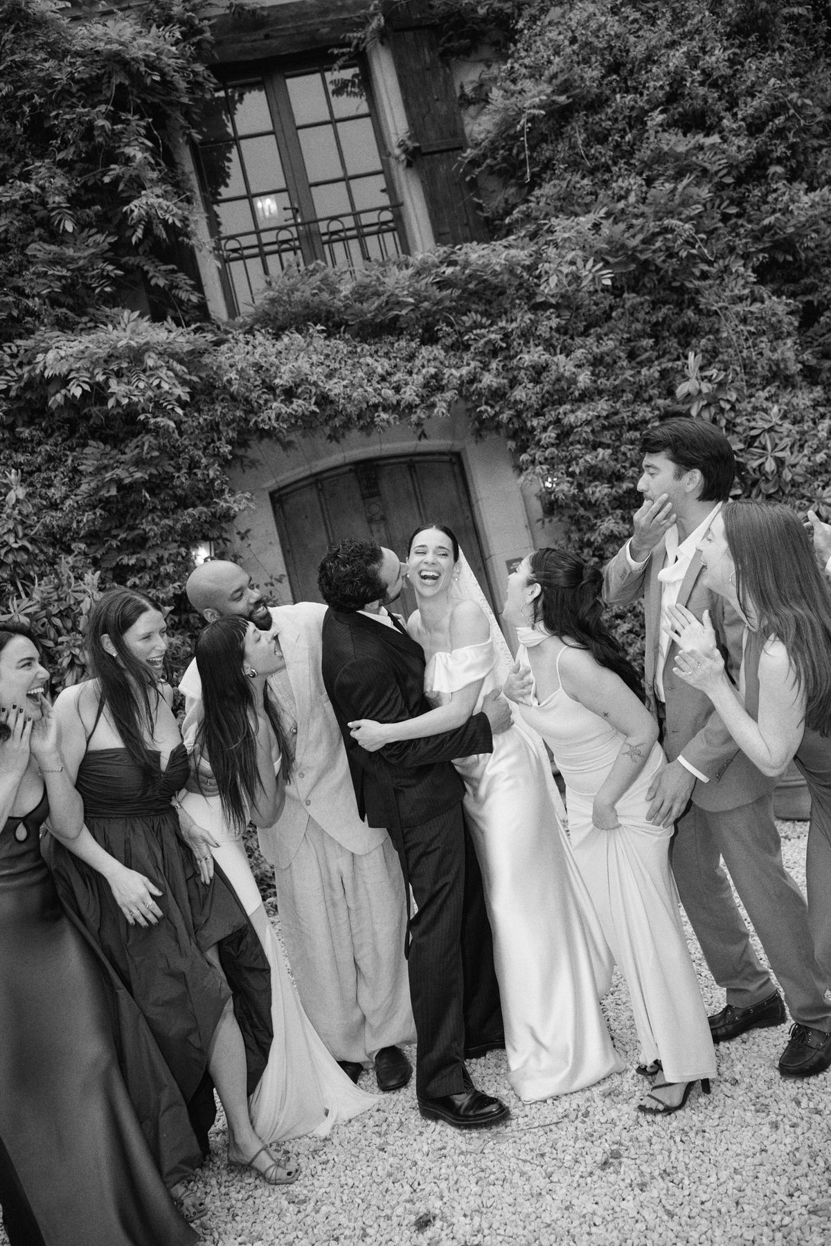 The bride laughing among her wedding party outside an ivy-covered doorway