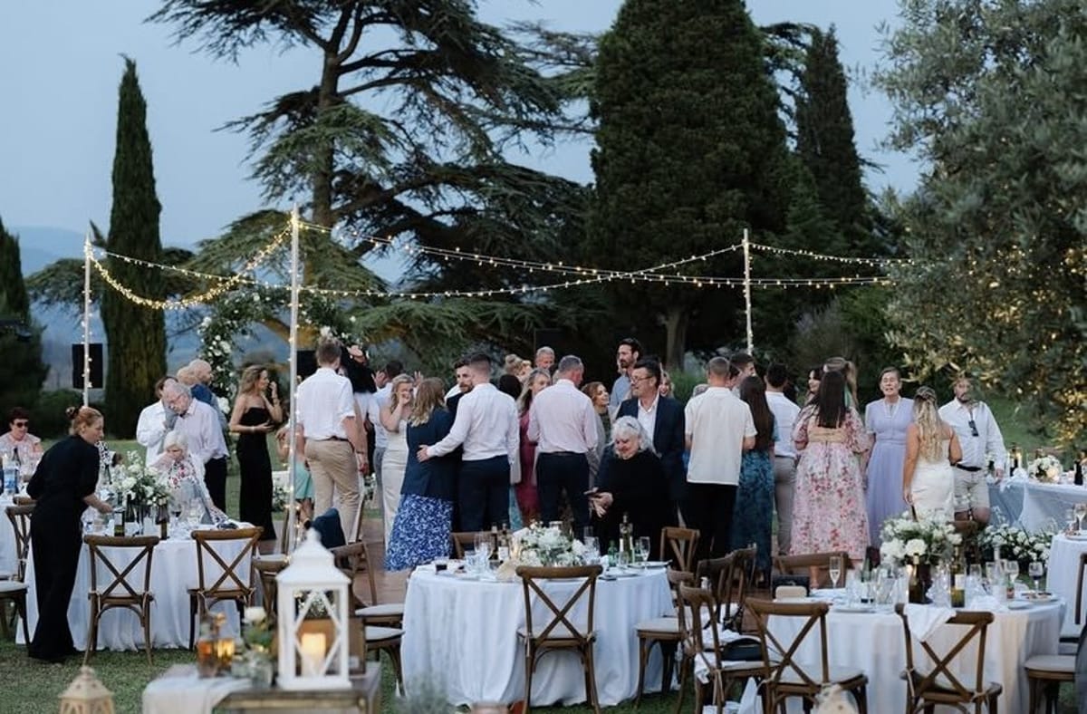 Round tables and festoon lights on the lawn at dusk as guests gather for the evening reception