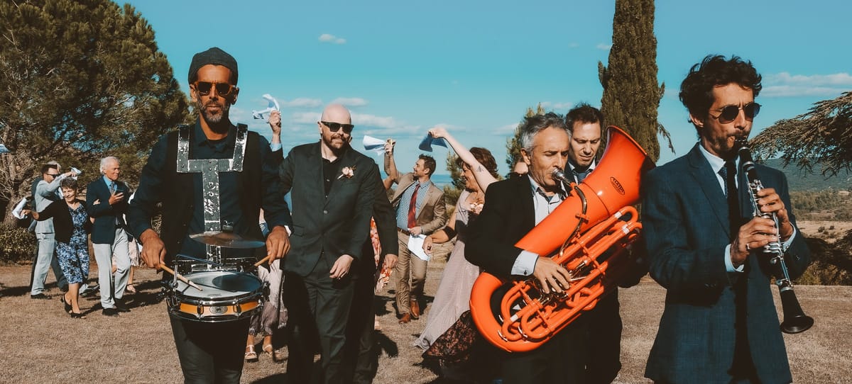 A brass band leads guests across the grounds, tuba and clarinet out in front