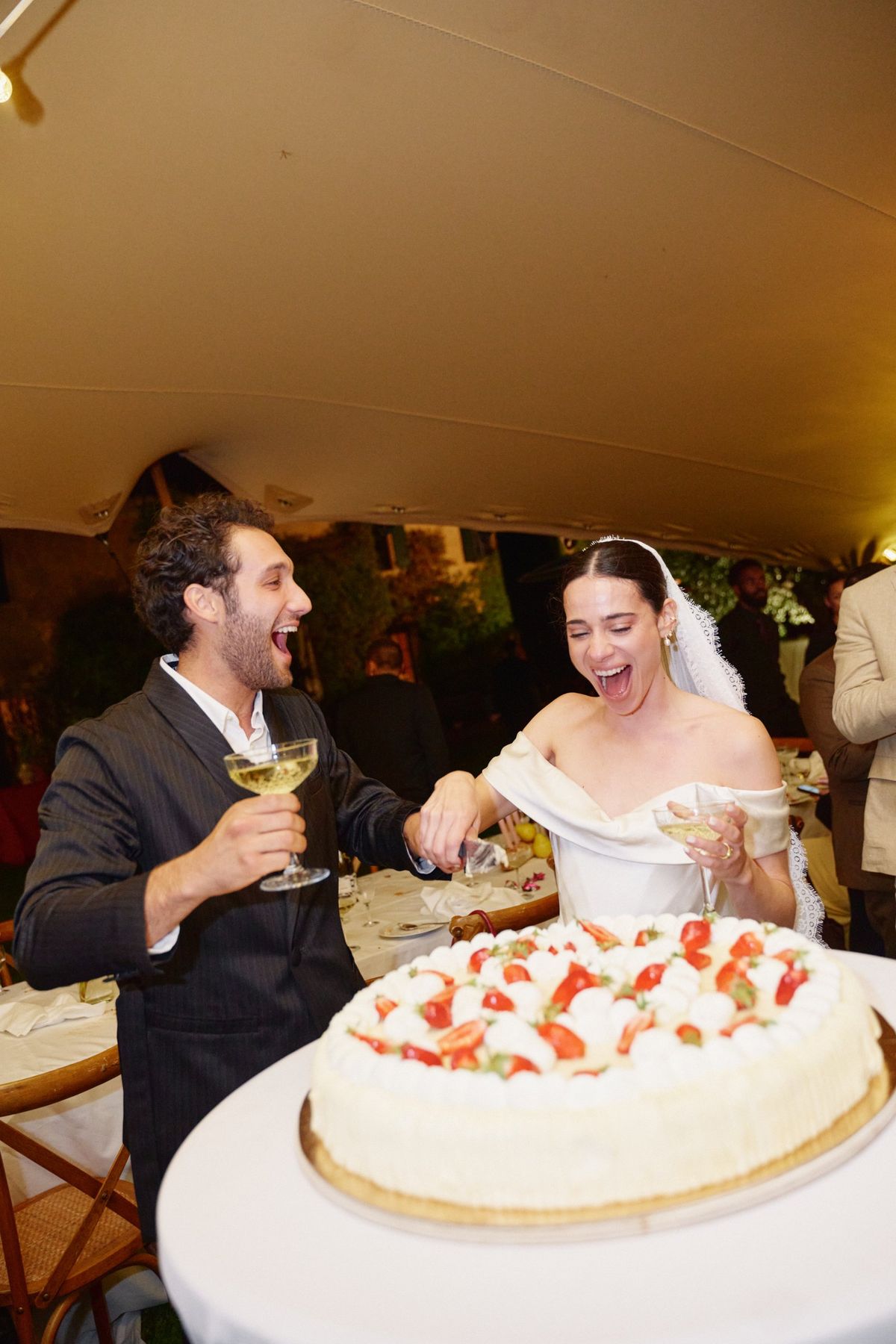 Bride and groom laughing as they cut their strawberry cream cake under the marquee