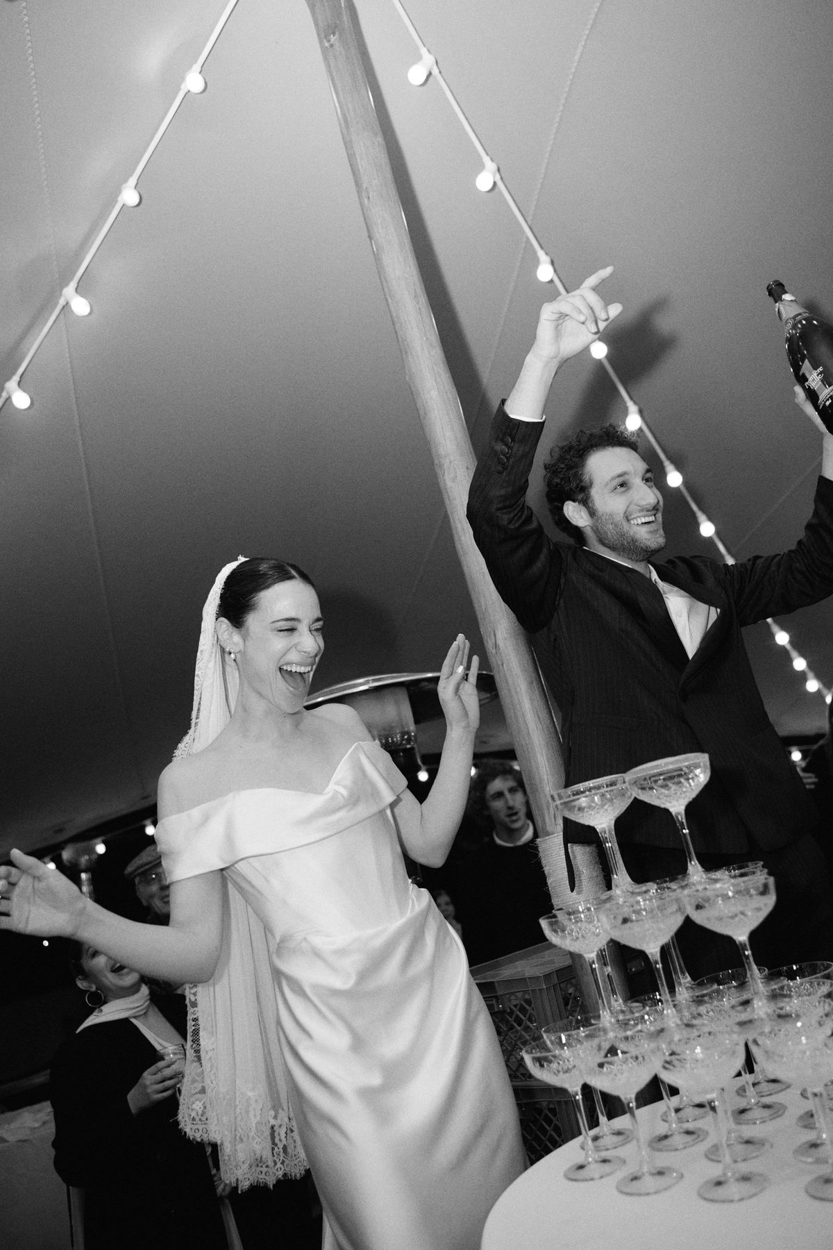 Bride and groom celebrate beside the champagne tower under the marquee