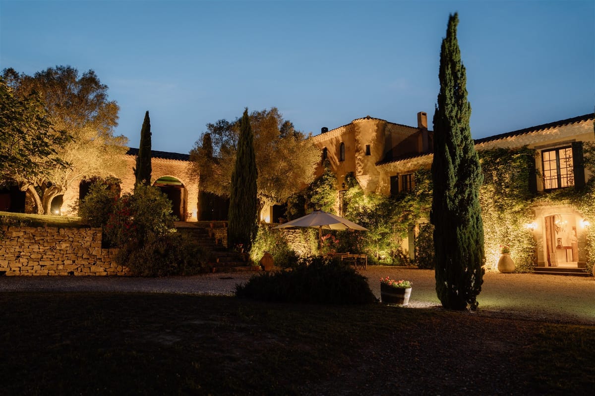 The house lit at night, cypresses and the gravel courtyard under a deep blue sky