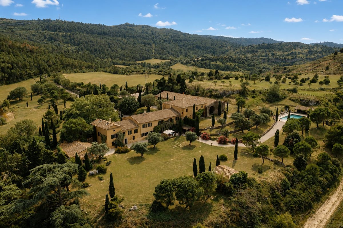 Aerial view of the estate, its ranges of buildings, lawns and cypress avenues among wooded hills